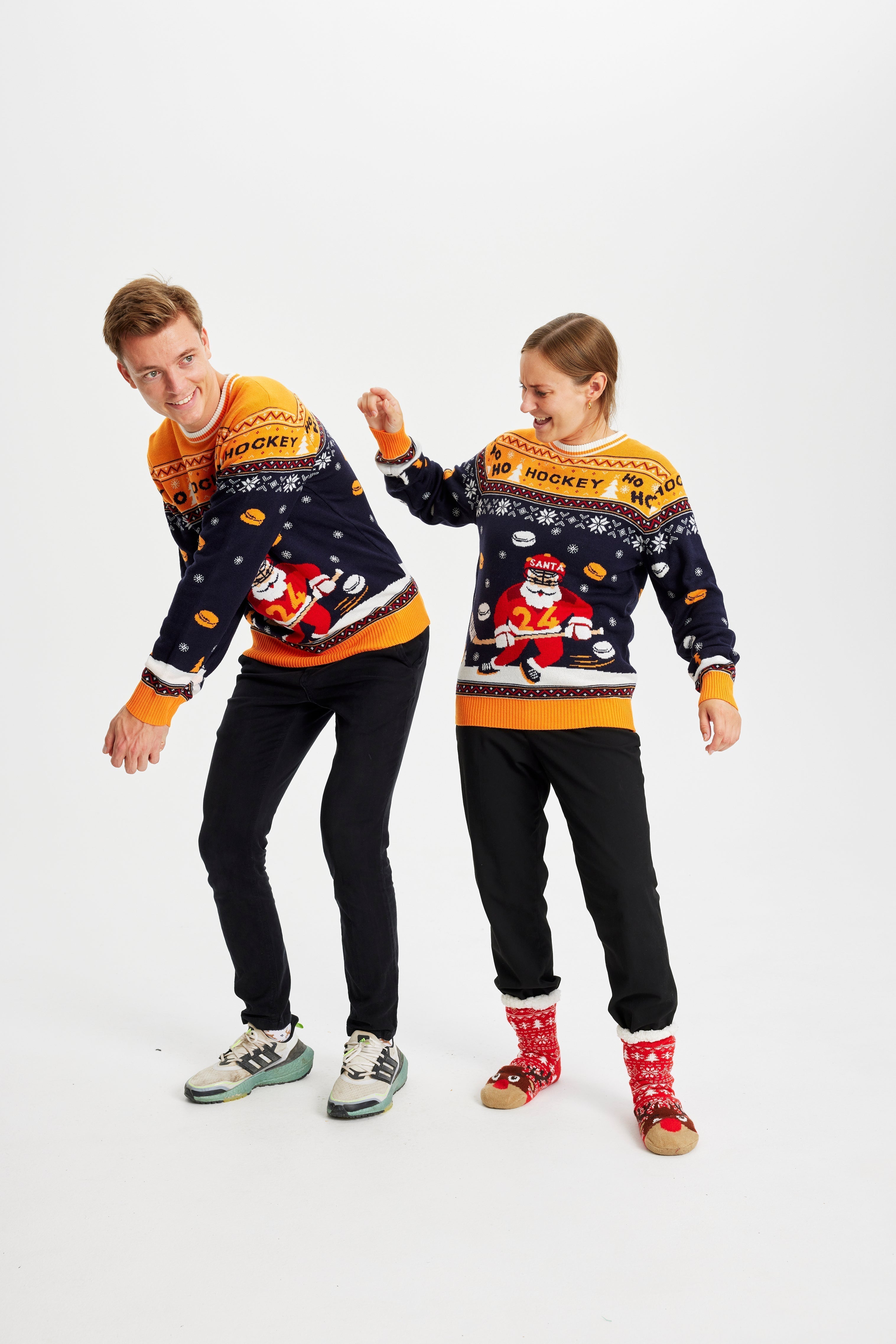 Una coppia in posa che indossa un maglione natalizio giallo e blu con sopra un Babbo Natale che gioca a hockey.